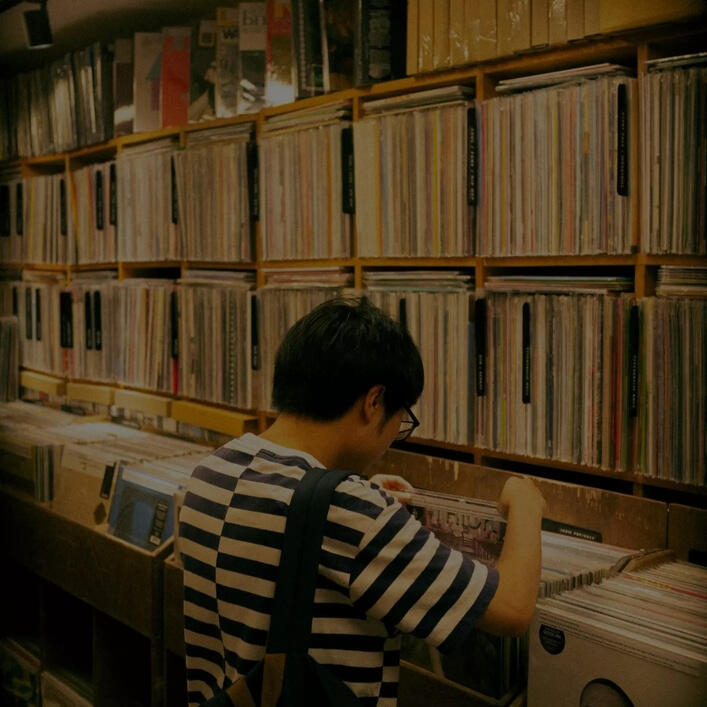 Person browsing through vinyl records in a record store, standing in front of shelves filled with neatly organized LPs.