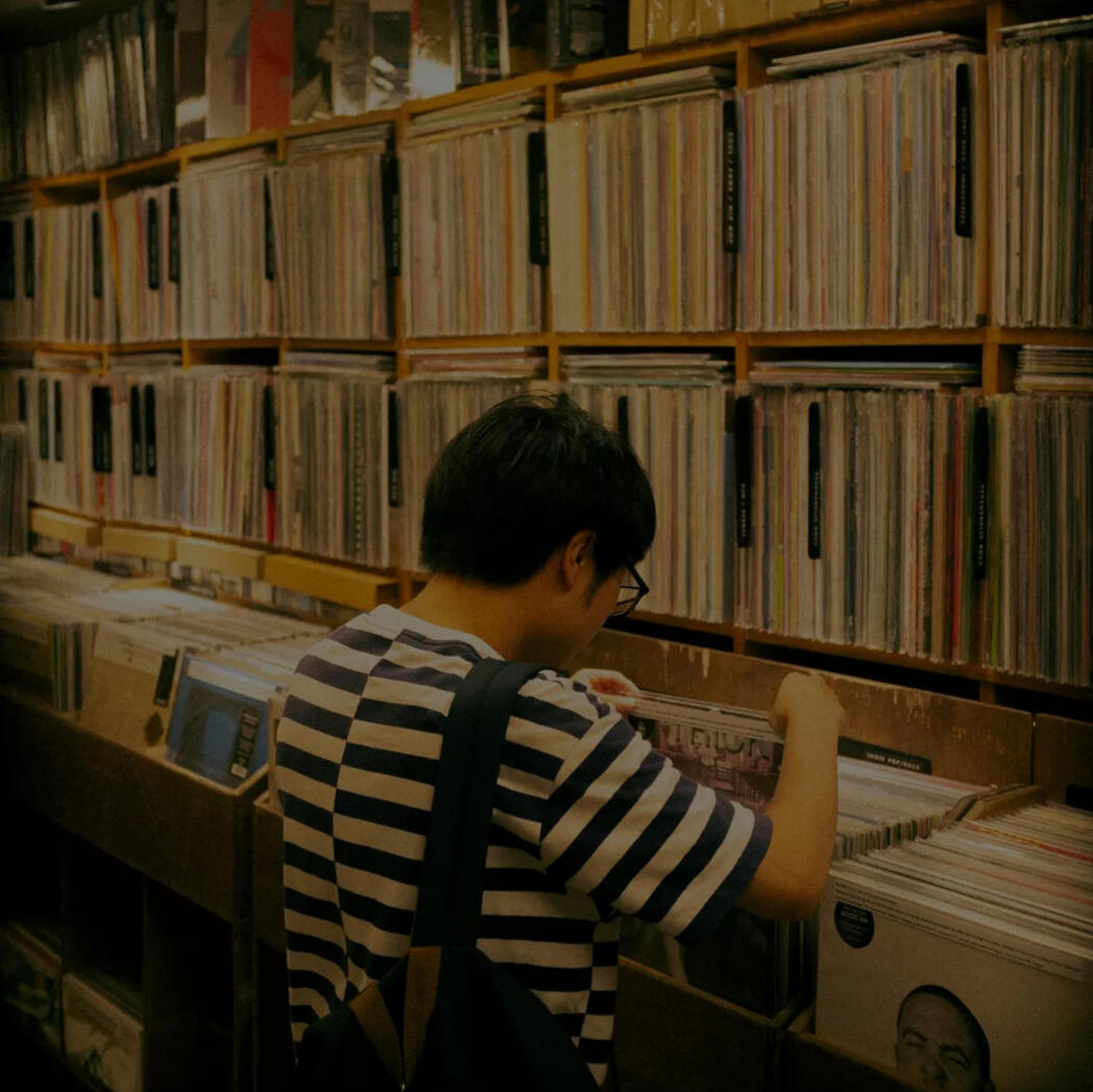 Person browsing through vinyl records in a record store, standing in front of shelves filled with neatly organized LPs.